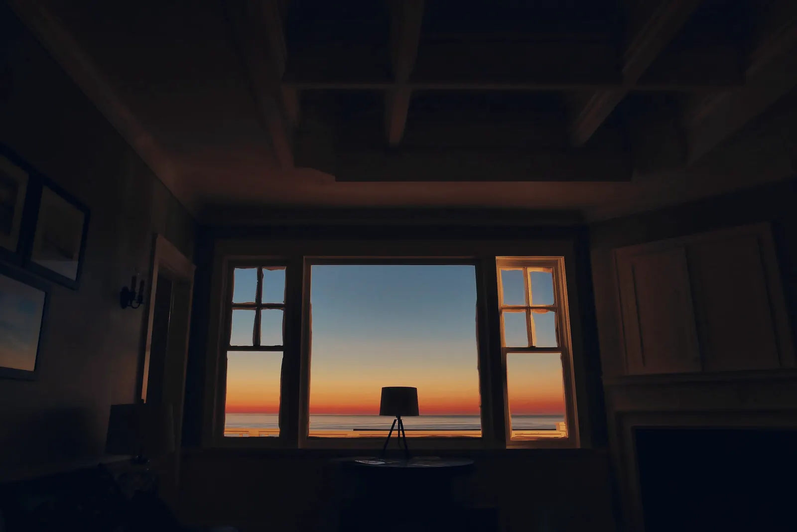 Salón en penumbra; al fondo, un ventanal enmarca la puesta de sol sobre el mar.